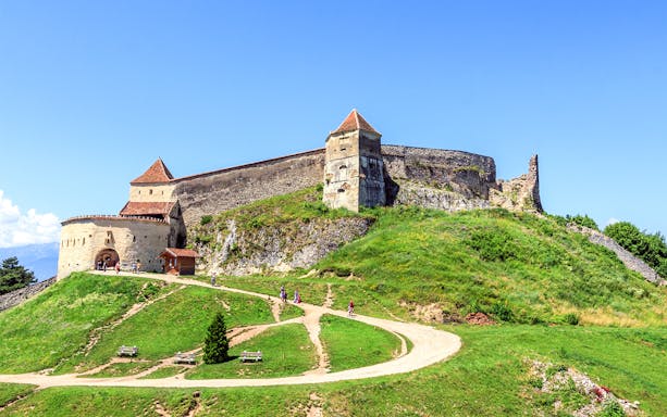 Medieval fortress on a hill with tourists walking, near Bran Castle, Romania.