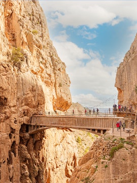 Visitors walking along the narrow path of Caminito Del Rey in Malaga, surrounded by steep cliffs.