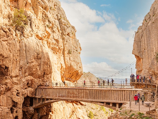 Visitors walking along the narrow path of Caminito Del Rey in Malaga, surrounded by steep cliffs.