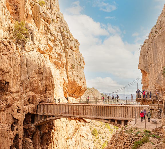 Visitors walking along the narrow path of Caminito Del Rey in Malaga, surrounded by steep cliffs.