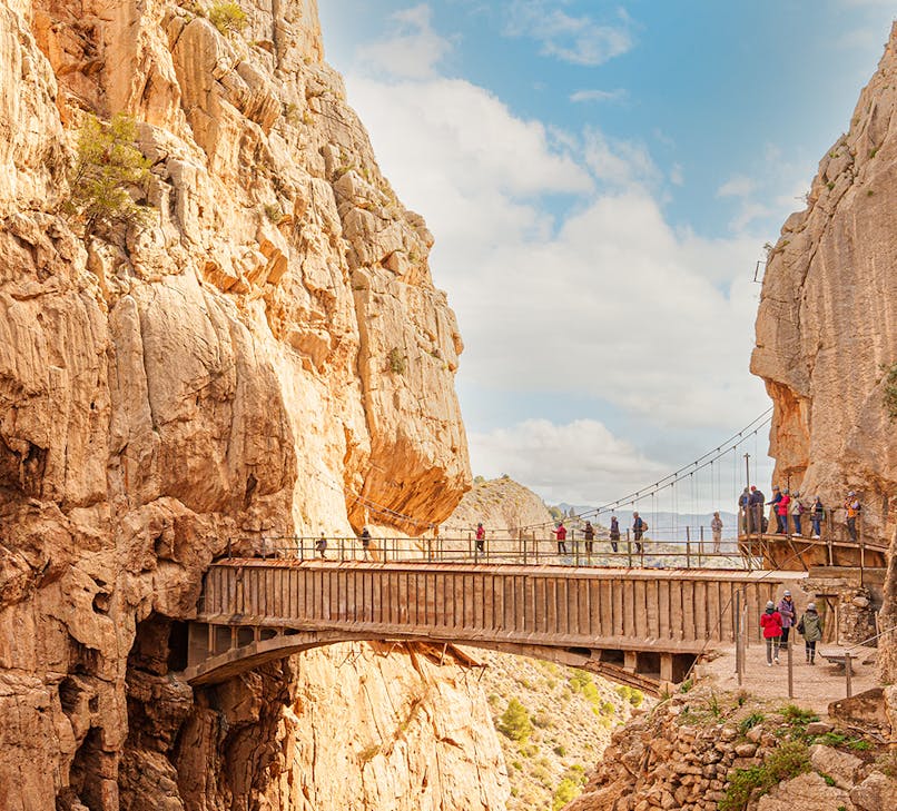 Caminito Del Rey walkway in Malaga, Spain, with hikers on a narrow path along a steep cliff.