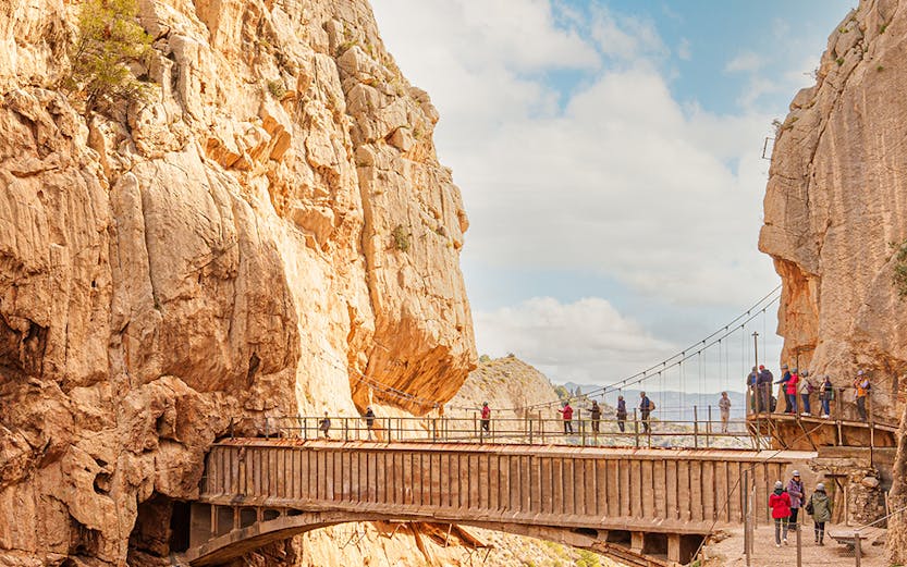 Visitors walking along the narrow path of Caminito Del Rey in Malaga, surrounded by steep cliffs.