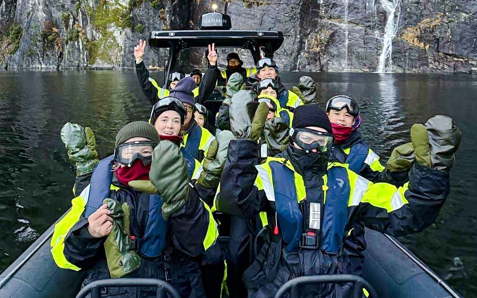 Guests on a RIB boat enjoying Alversund Fjord Safari with cliffs and waterfall in the background.