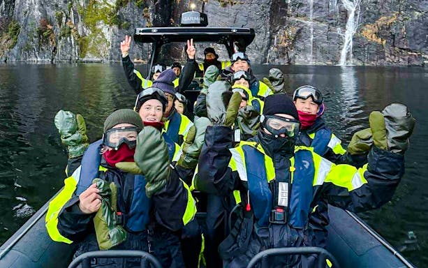Guests on a RIB boat enjoying Alversund Fjord Safari with cliffs and waterfall in the background.