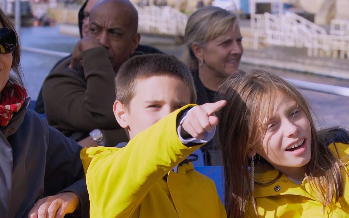 Children in yellow jackets enjoying a York sightseeing cruise, pointing at landmarks.