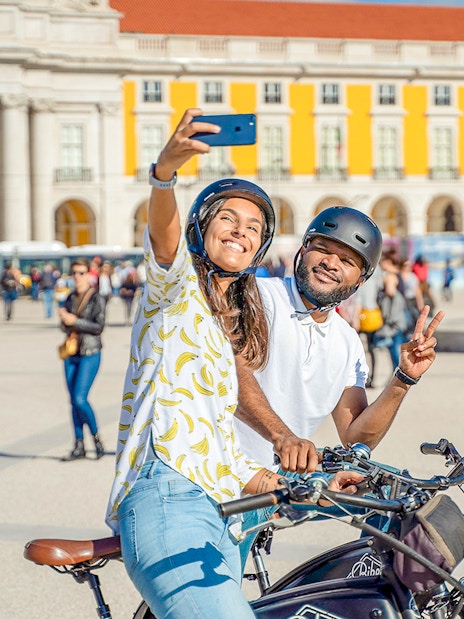 Tourists on electric bikes taking selfie at Praça do Comércio, Lisbon, Portugal.