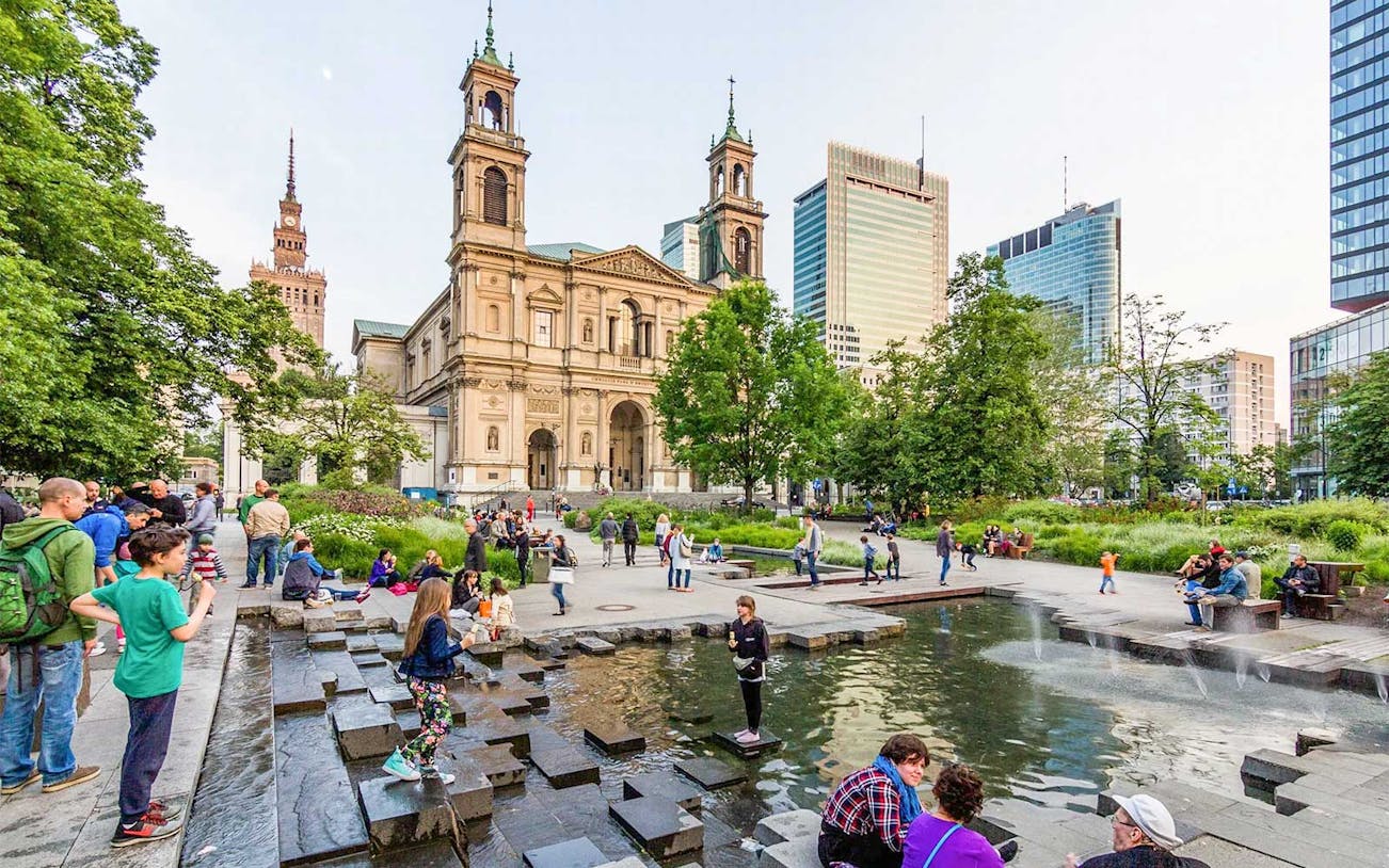 People enjoying a park near a historic church in Warsaw during a Jewish heritage walking tour.