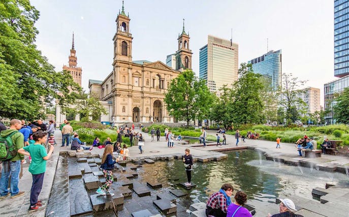 People enjoying a park near a historic church in Warsaw during a Jewish heritage walking tour.