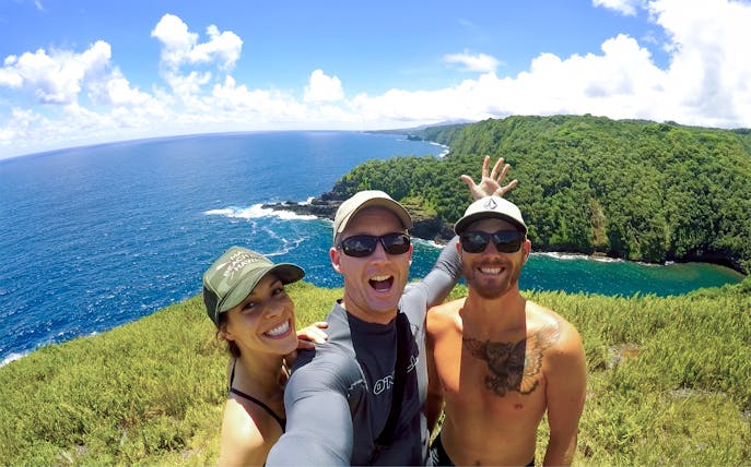 Group enjoying scenic view on Road to Hana, Maui, Hawaii, with ocean and lush cliffs in background.