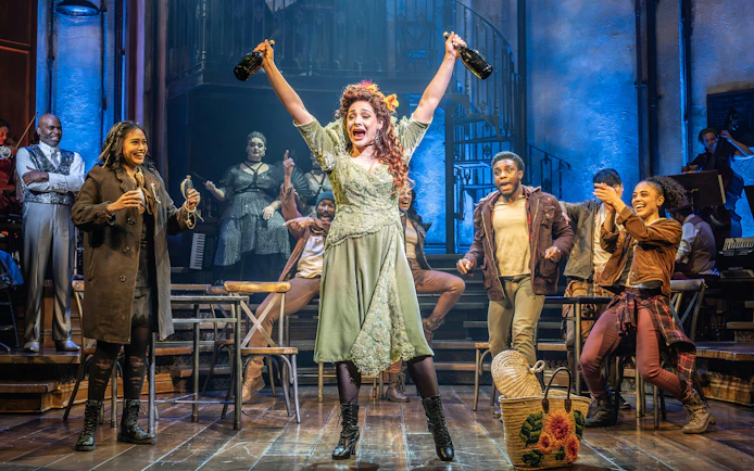 Stage performance of Hadestown in West End with actors celebrating on stage.