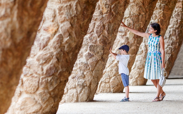 Mother and son exploring stone columns in Park Guell, Barcelona.