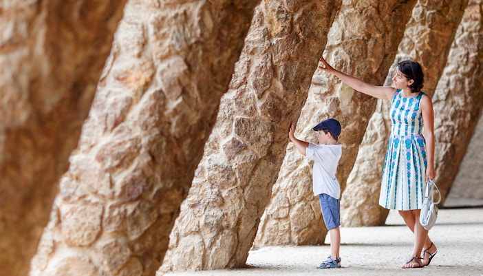 Mother and son walking through colorful mosaic structures in Park Guell, Barcelona.