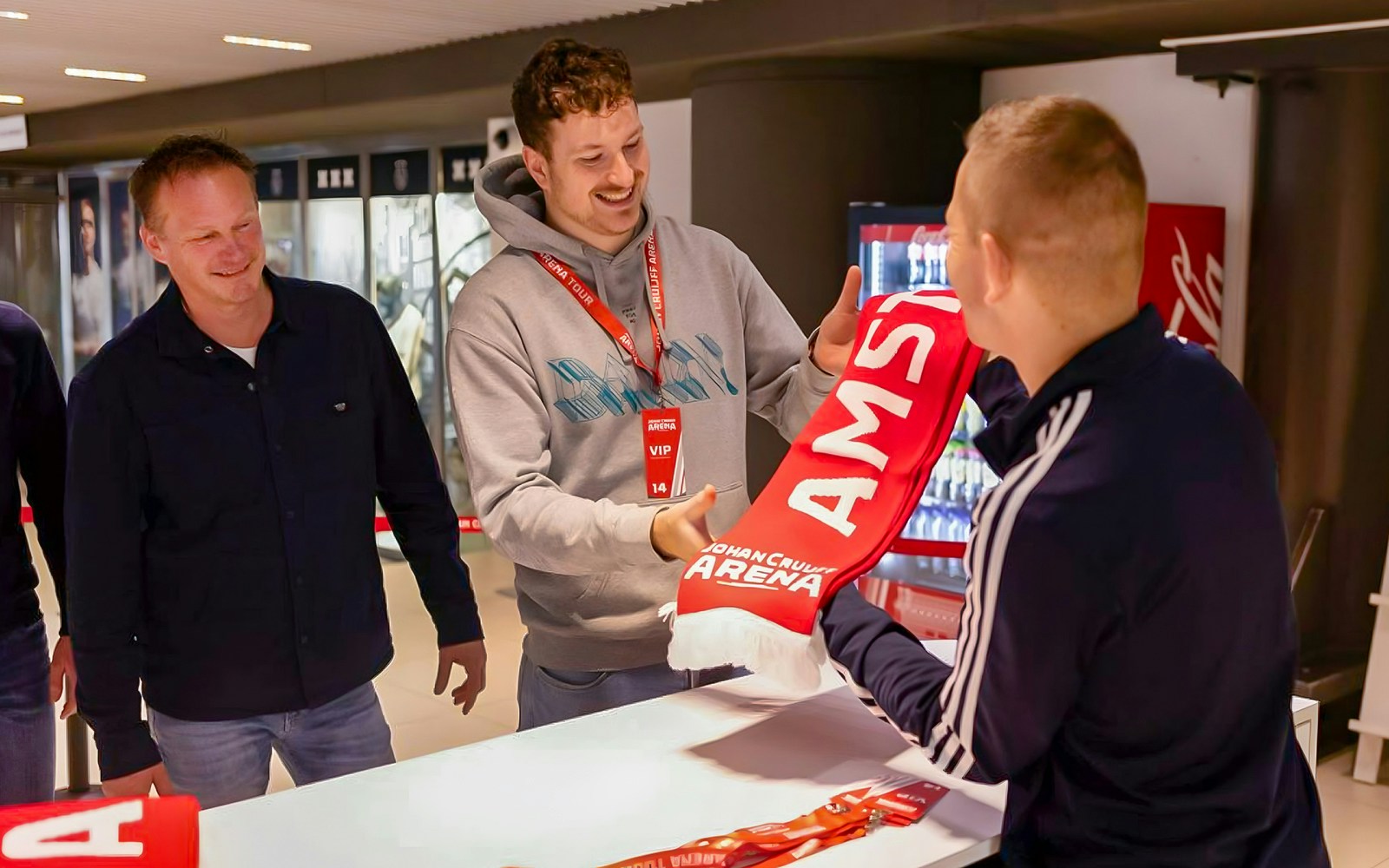 Visitors on a VIP tour at Johan Cruijff ArenA, Amsterdam, holding drinks and scarves.
