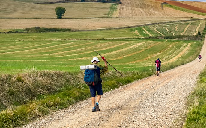 Hikers on a gravel path through fields on St James Way from San Sebastian to San Pedro.