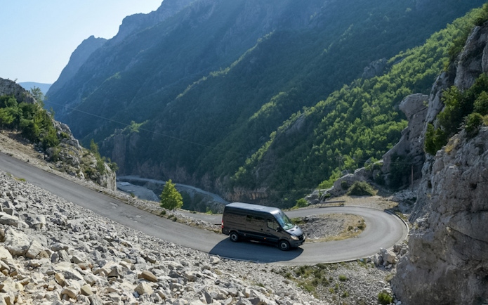 Van on winding road with Gamti Mountain backdrop, used for Bovilla Lake & Gamti Mountain Hiking Tour.