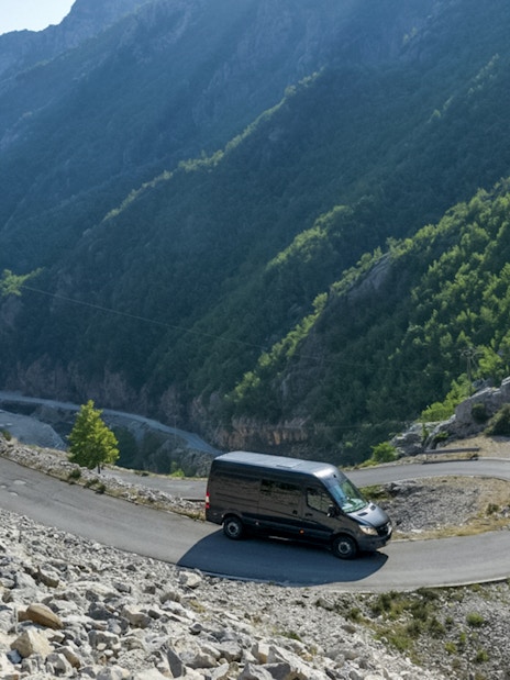 Van on winding road with Gamti Mountain backdrop, used for Bovilla Lake & Gamti Mountain Hiking Tour.