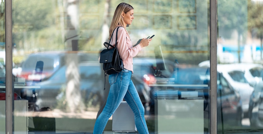 Woman walking in city while using smartphone, reflecting urban lifestyle.