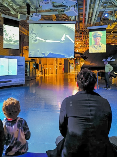 Visitors watching historical footage at a museum exhibit with multiple screens.