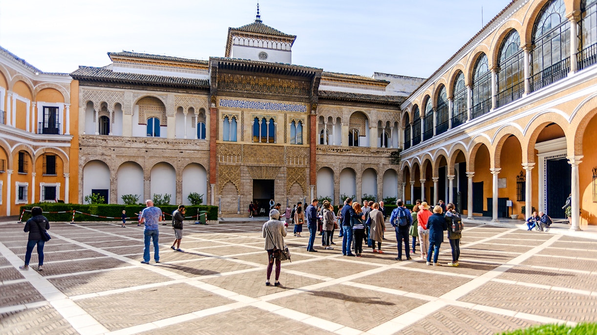 Tourists exploring the courtyard of Alcázar in Seville.