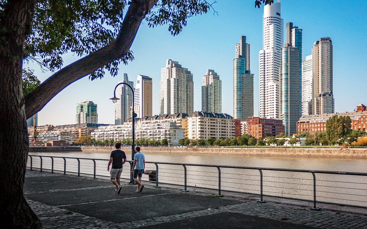 Buenos Aires river walk with people strolling and city skyline in the background.