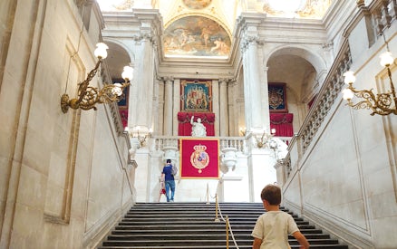 Grand staircase inside Royal Palace of Madrid with visitors ascending.
