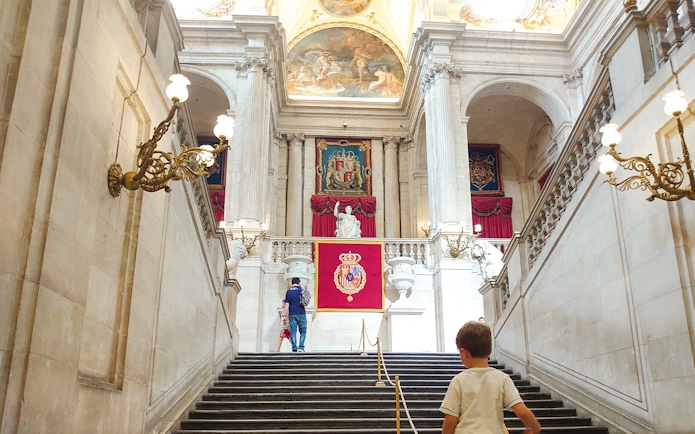 Grand staircase inside Royal Palace of Madrid with visitors ascending.