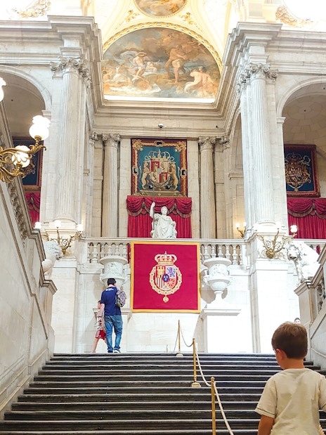 Grand staircase inside Royal Palace of Madrid with visitors ascending.