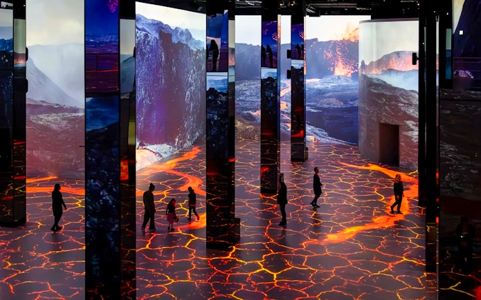 Guests exploring immersive Dinosaurs exhibition at Phoenix des Lumières Dortmund with volcanic visuals.