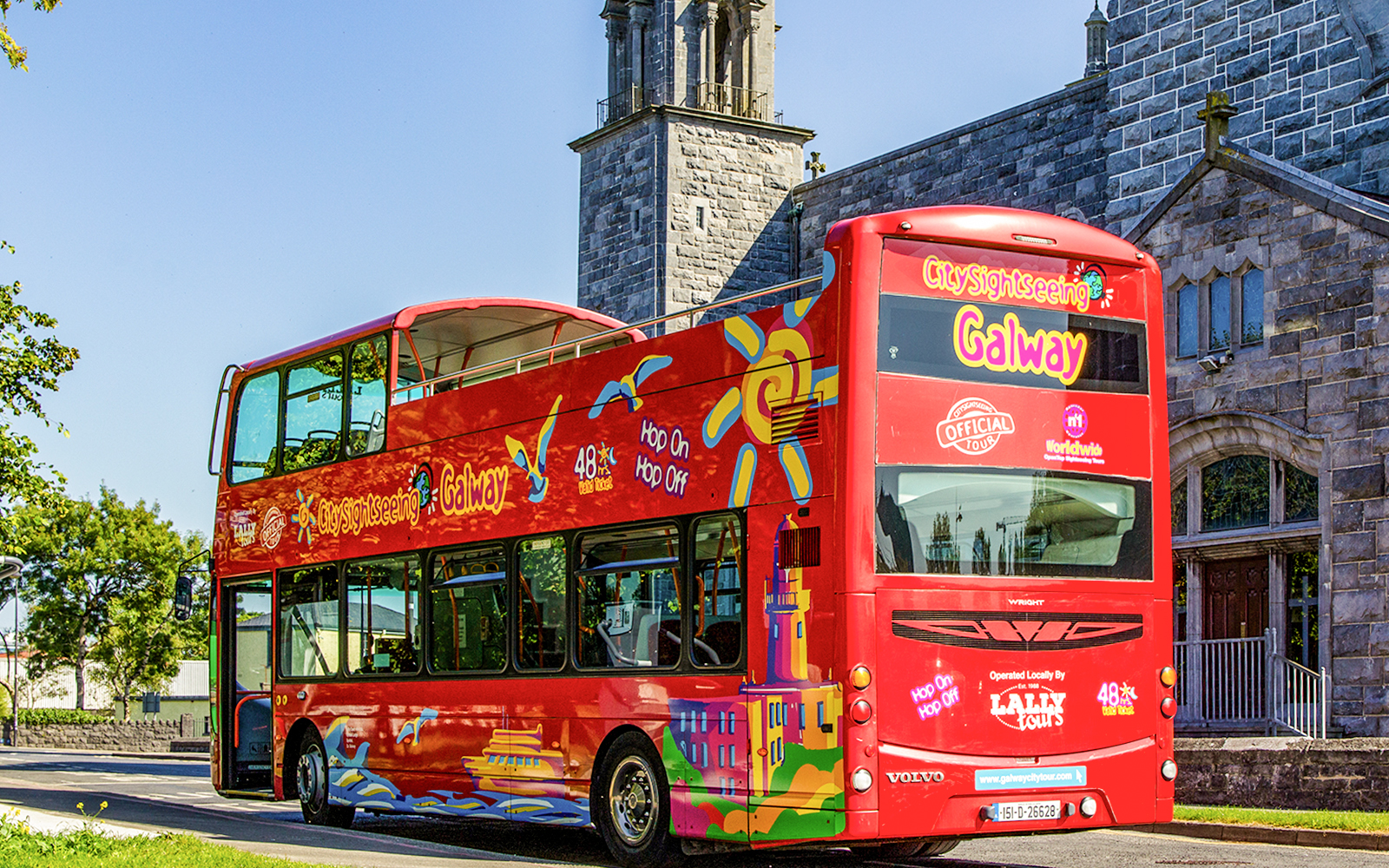 Red double-decker bus for Galway Hop-On-Hop-Off Tour near historic stone building.