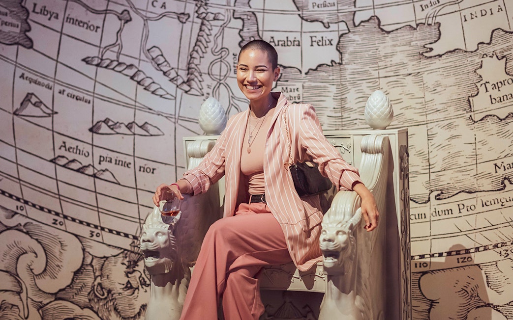 Smiling visitor seated on ornate chair at Pink Palace with historical map backdrop.