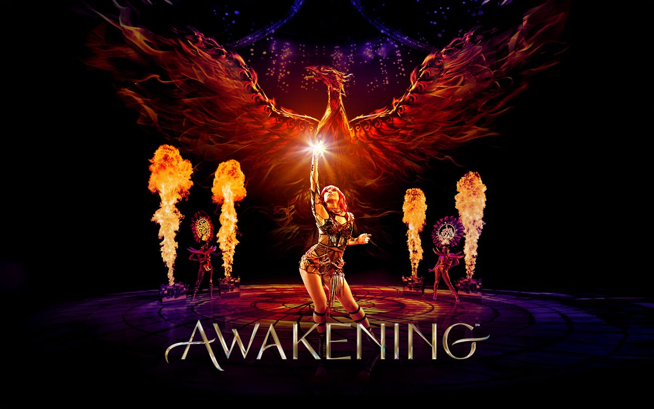Performer reaching towards a fiery phoenix with flames and dancers in the Awakening show.