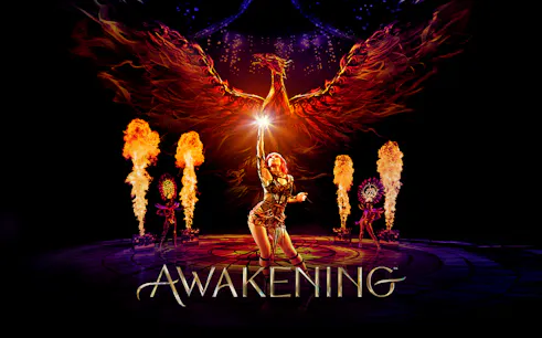 Performer reaching towards a fiery phoenix with flames and dancers in the Awakening show.