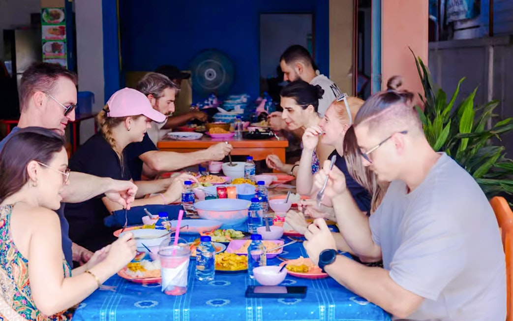 Tourists dining at a Thai buffet, enjoying various dishes at a communal table.