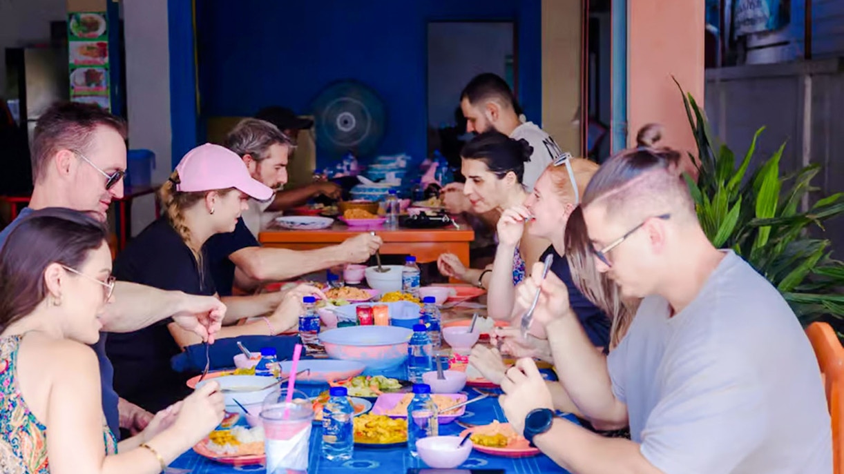 Tourists dining at a Thai buffet, enjoying various dishes at a communal table.