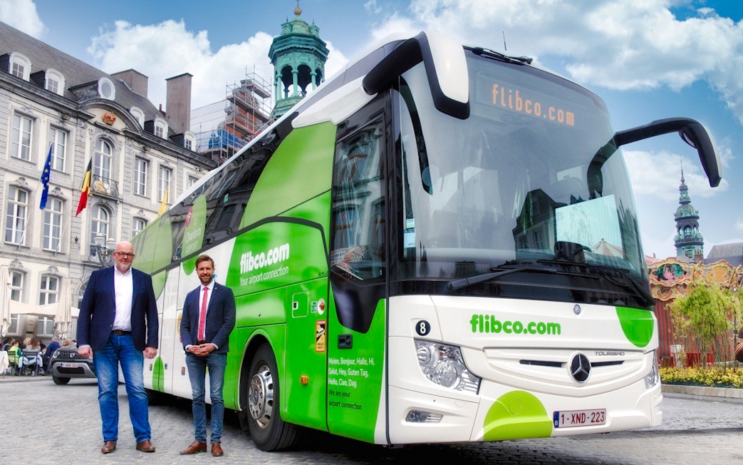 Bus driver posing with green and white tour bus in London.