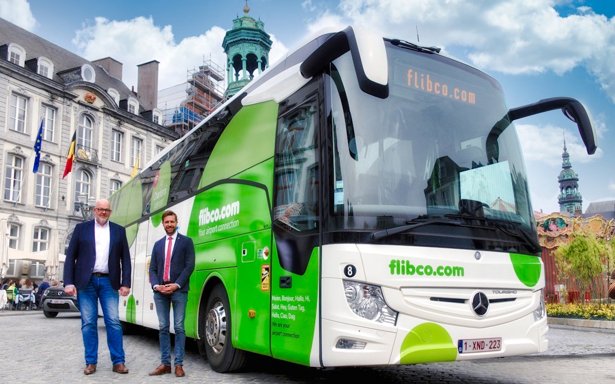 Bus driver posing with green and white tour bus in London.