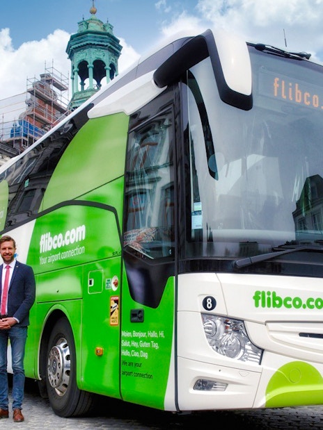 Bus driver posing with green and white tour bus in London.