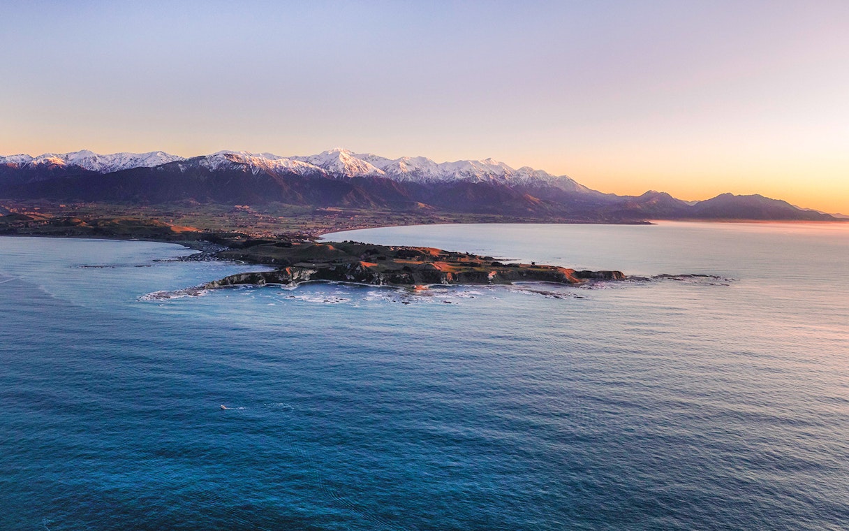 Aerial view of Kaikoura coastline with snowy mountains in the background.