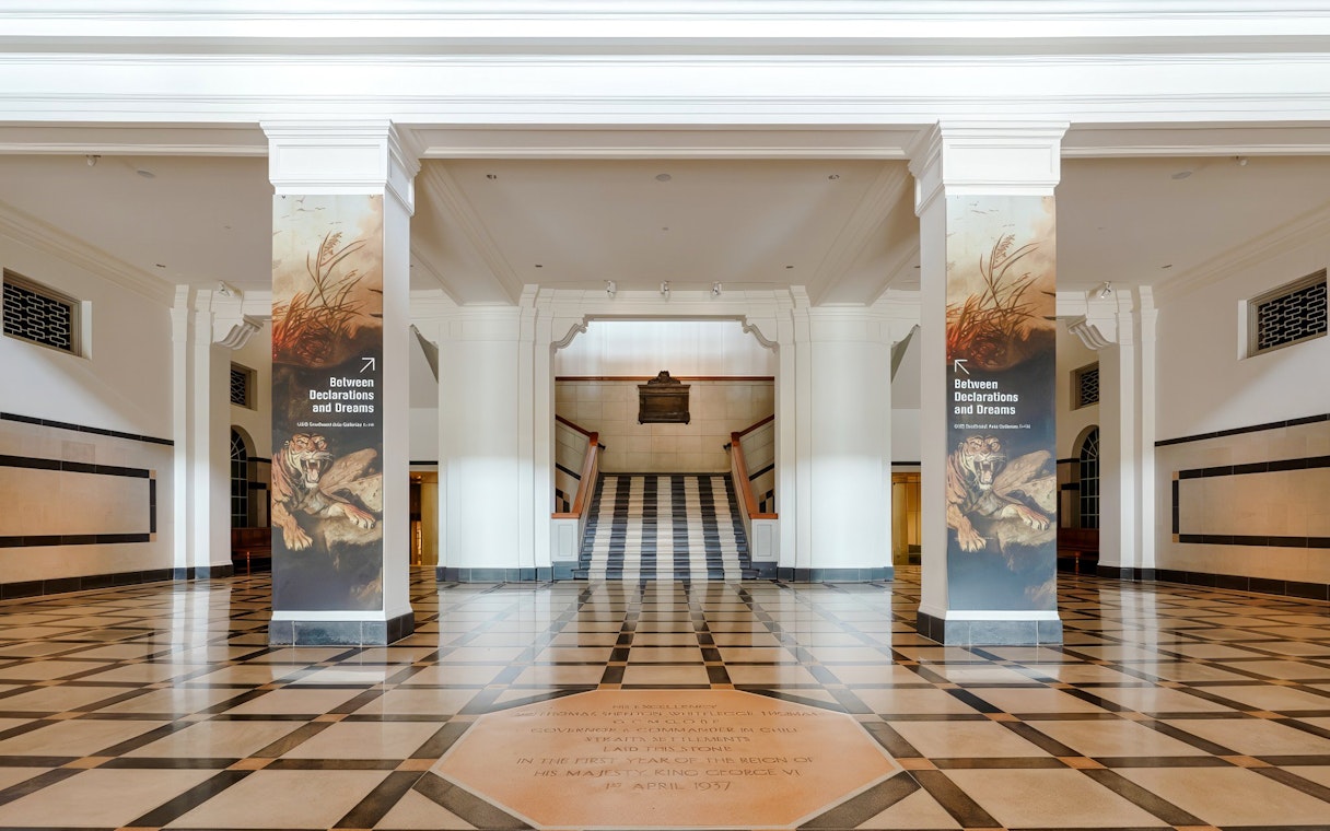 Hallway with columns and "Between Declarations and Dreams" banners, National Gallery Singapore.