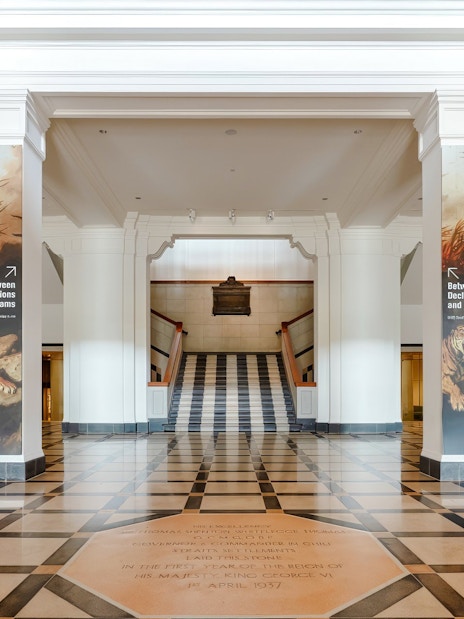 Hallway with columns and "Between Declarations and Dreams" banners, National Gallery Singapore.