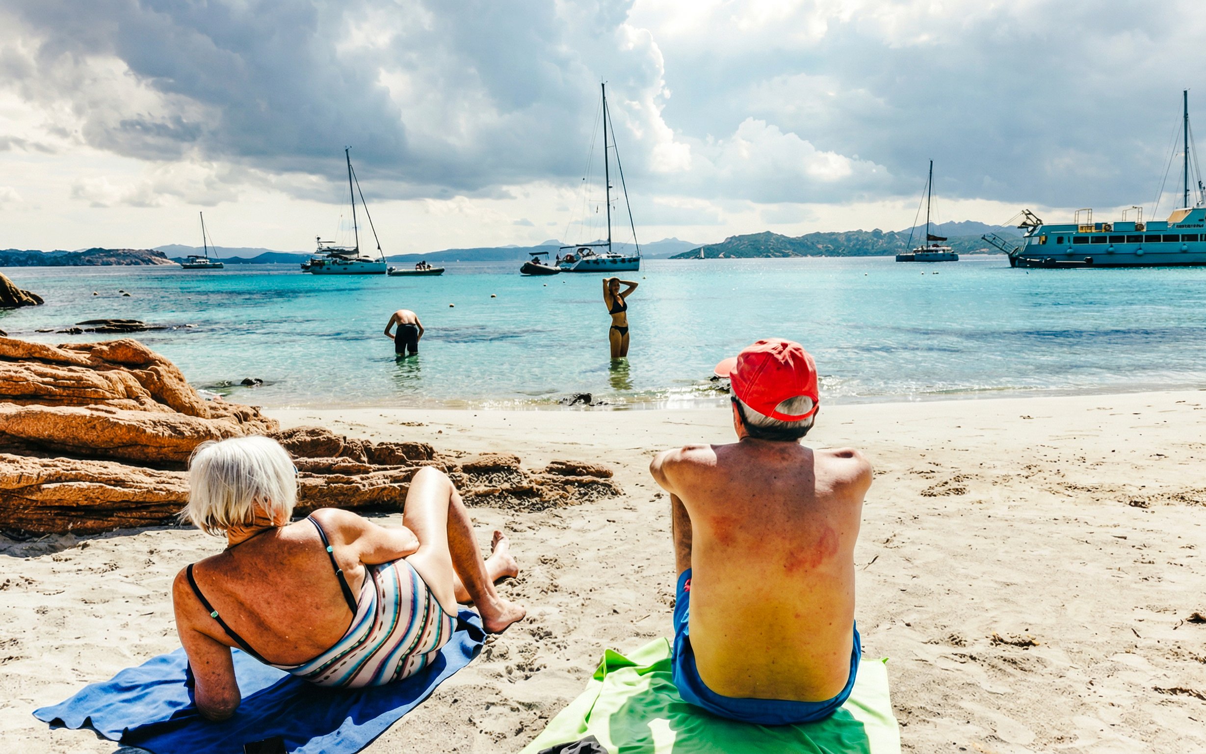 Beachgoers relaxing on the shore with sailboats in La Maddalena Archipelago.