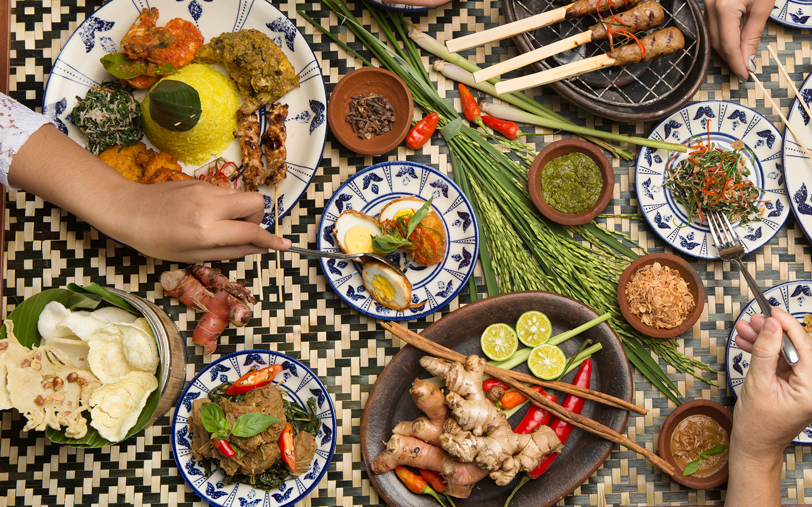 Balinese dishes with rice, satay, and spices on a woven table in Bali.