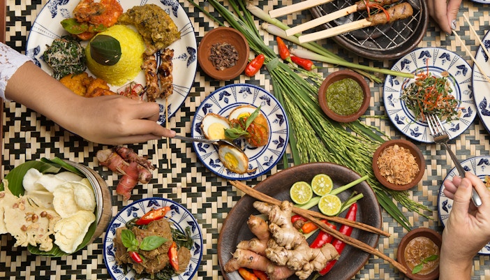 Balinese dishes with rice, satay, and spices on a woven table in Bali.