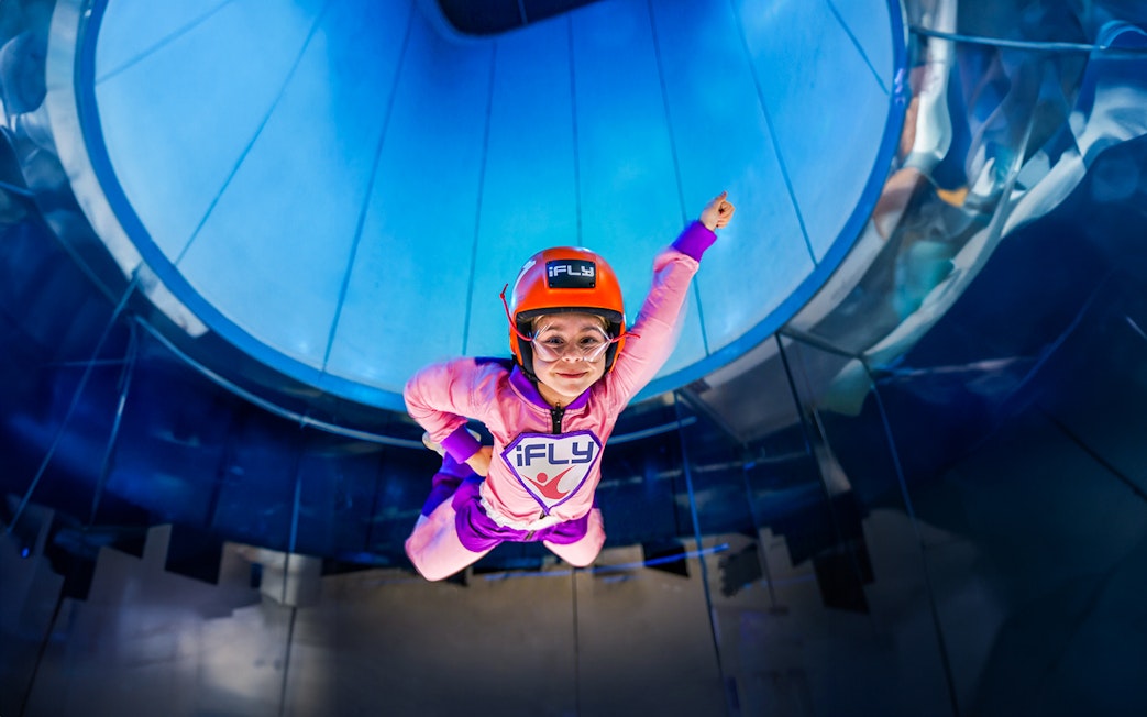 Child enjoying iFLY indoor skydiving experience in a wind tunnel.