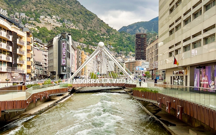 River flowing through Andorra la Vella's urban center with a white suspension bridge.