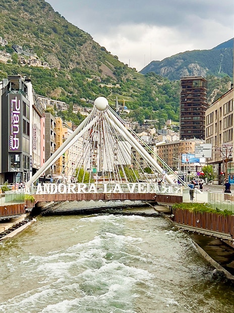 River flowing through Andorra la Vella's urban center with a white suspension bridge.