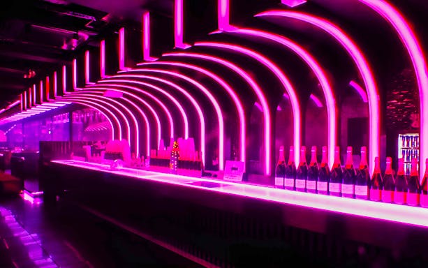 Neon-lit bar inside KITSUNE Kyoto Nightclub with rows of bottles.