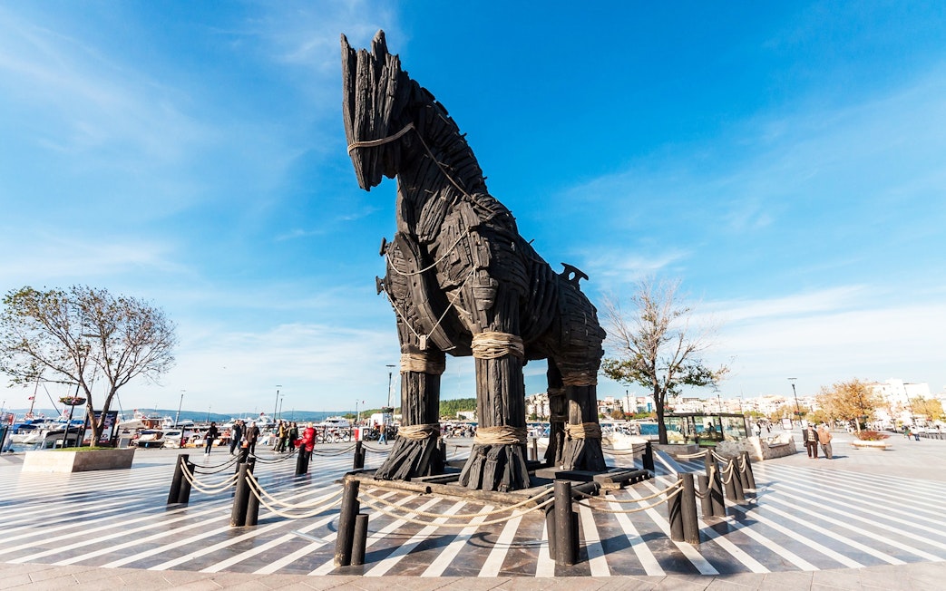 Trojan Horse replica at Troy archaeological site, Turkey, with visitors exploring.