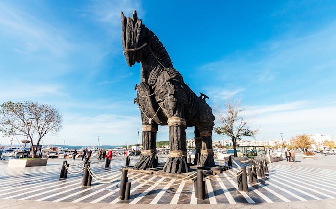 Trojan Horse replica at Troy archaeological site, Turkey, with visitors exploring.