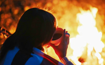 Girl enjoying warm drink by bonfire during Tromso Northern Lights tour.